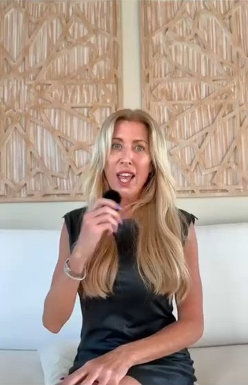 Erin Badour speaking into a handheld microphone in front of a carved wood panel